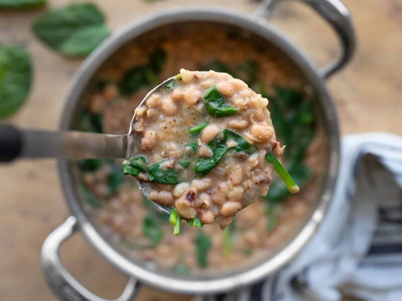 Close up of a ladle full of black eyed peas and greens with the pot in the background