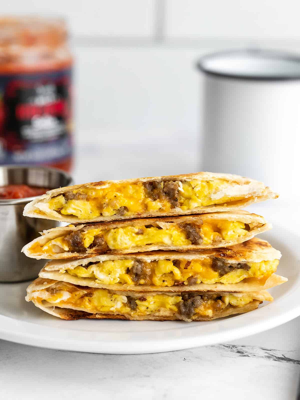 A stack of breakfast quesadillas on a plate with salsa in the background