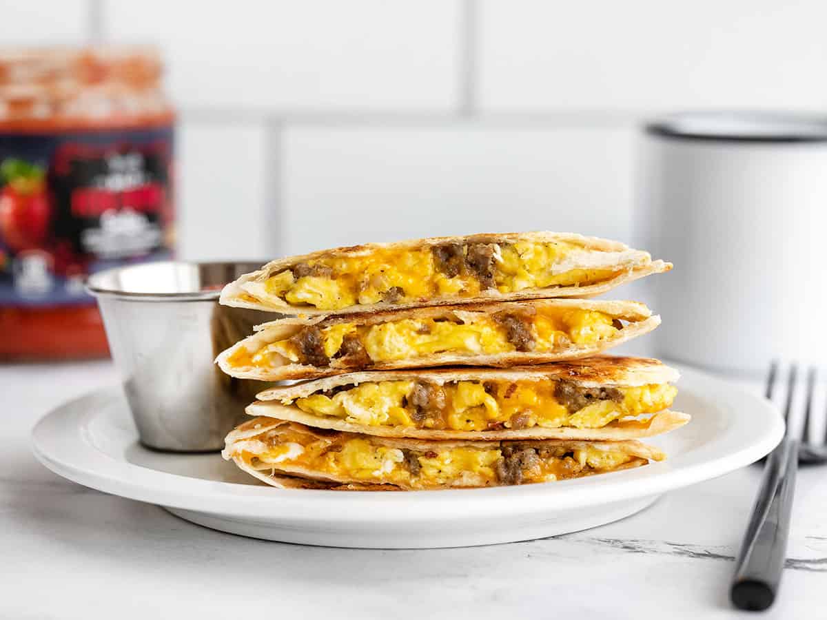 A stack of sausage and egg breakfast quesadillas on a plate with a dish of salsa
