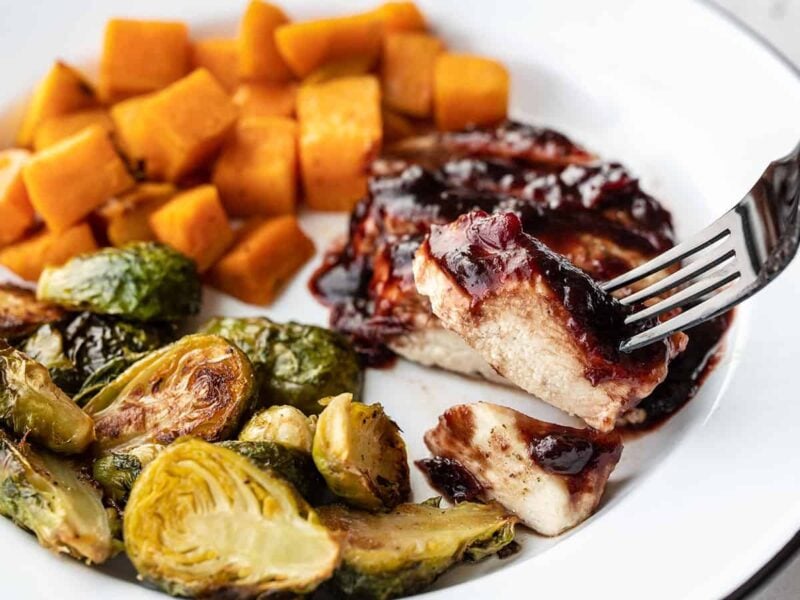 Sheet pan cranberry chicken dinner on a plate with a fork lifting a bite of chicken