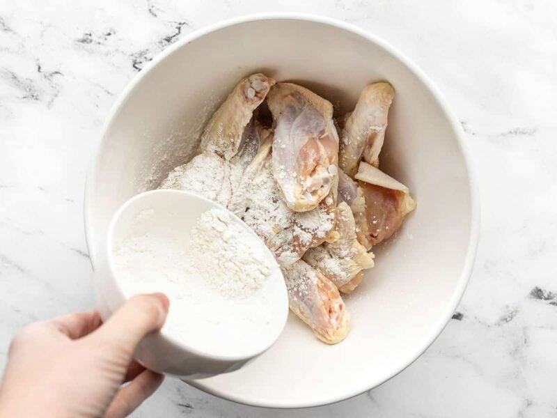 Cornstarch mixture being poured over the wings in a bowl