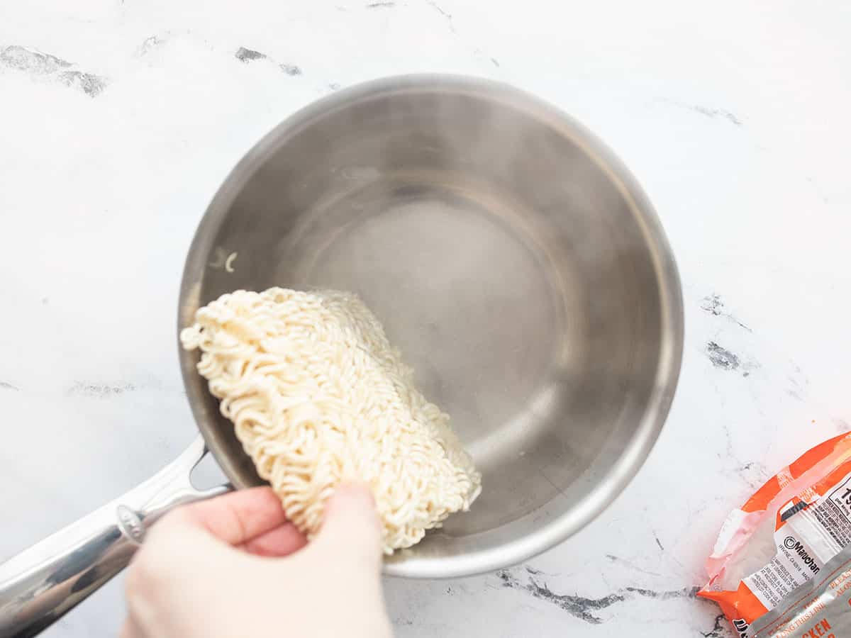 Dry ramen noodles being added to a pot of boiling water