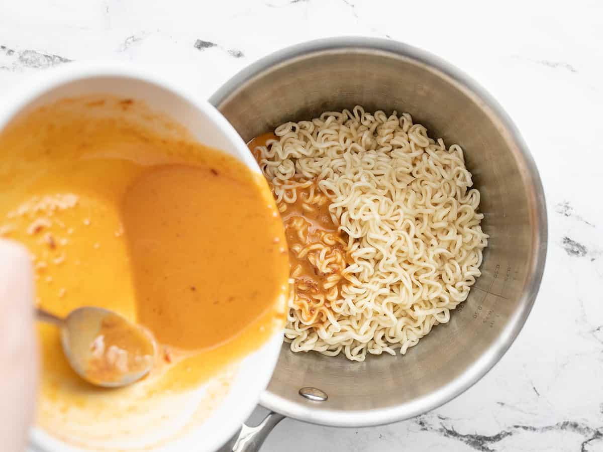 chili peanut sauce being poured over the drained ramen noodles