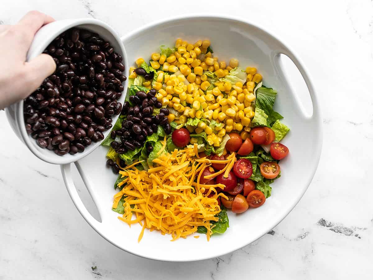 Beans being poured onto the salad with corn, tomatoes, and cheese