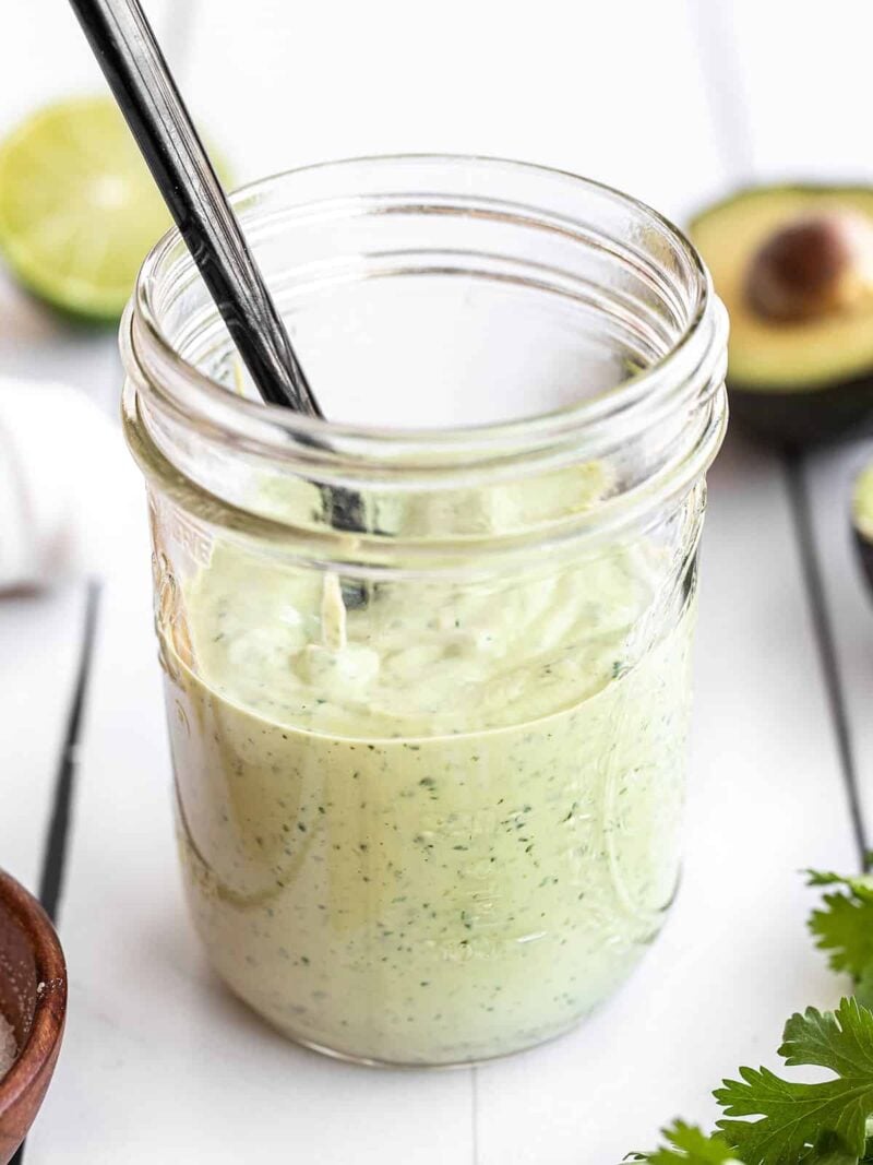 Creamy avocado dressing in a mason jar with a black spoon in the center