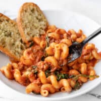 front view of a bowl full of creamy tomato pasta with sausage, a bit lifted on the fork