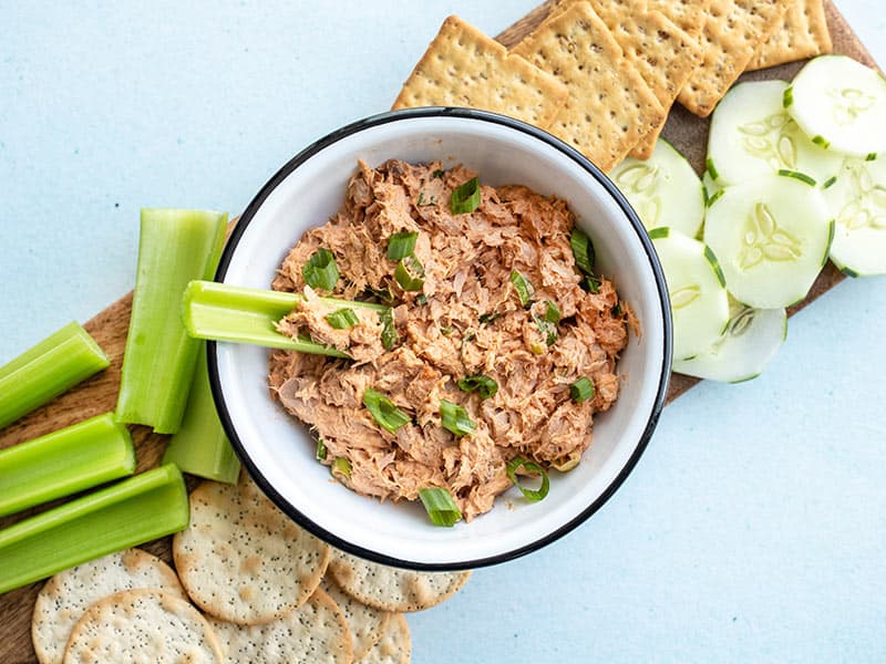 A bowl of gochujang tuna salad surrounded by vegetables and a celery stick dipped in the center