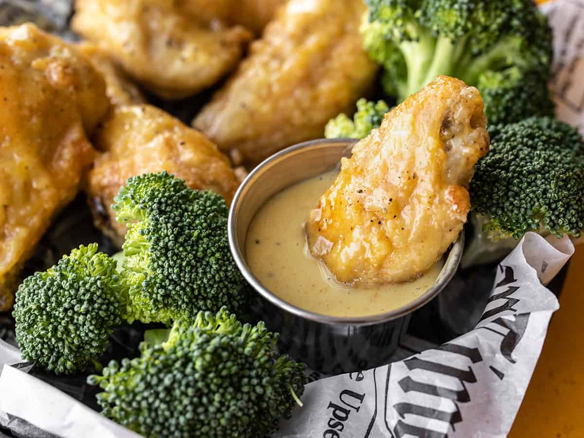 Close up of a honey mustard wing being dipped into a cup of honey mustard sauce