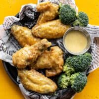 Overhead view of honey mustard wings on a tray with broccoli and a cup of sauce
