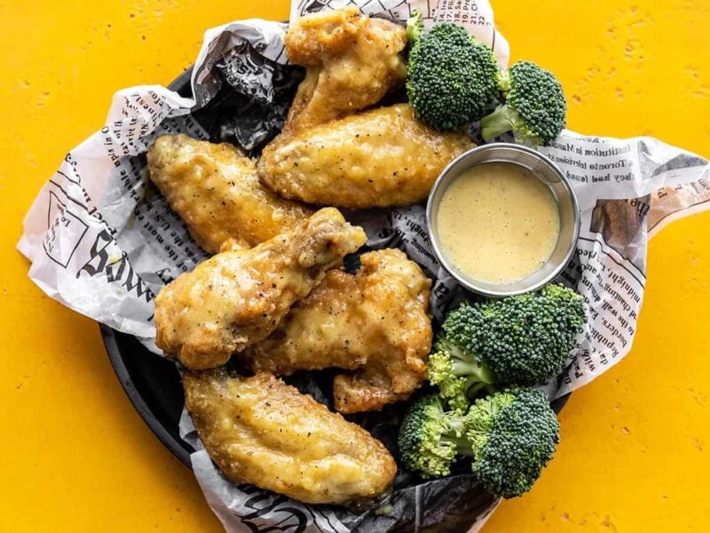 Overhead view of honey mustard wings on a tray with broccoli and a cup of sauce