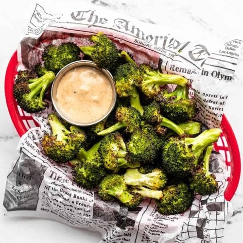Overhead view of a basket full of oven roasted broccoli with dipping sauce