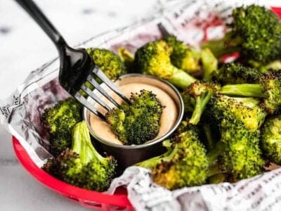 a piece of oven roasted broccoli being dipped into a cup of comeback sauce