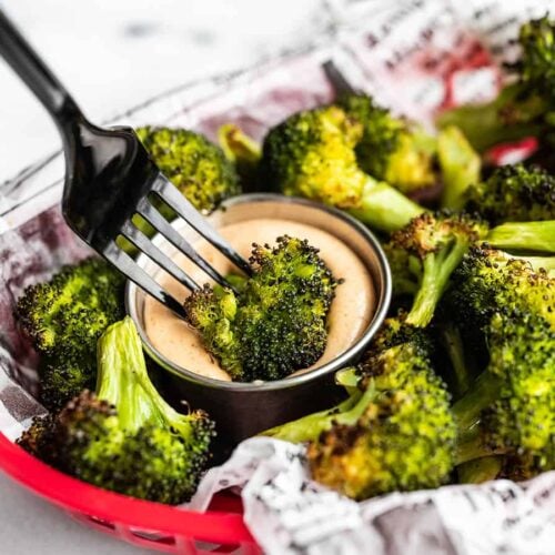 a piece of oven roasted broccoli being dipped into a cup of comeback sauce