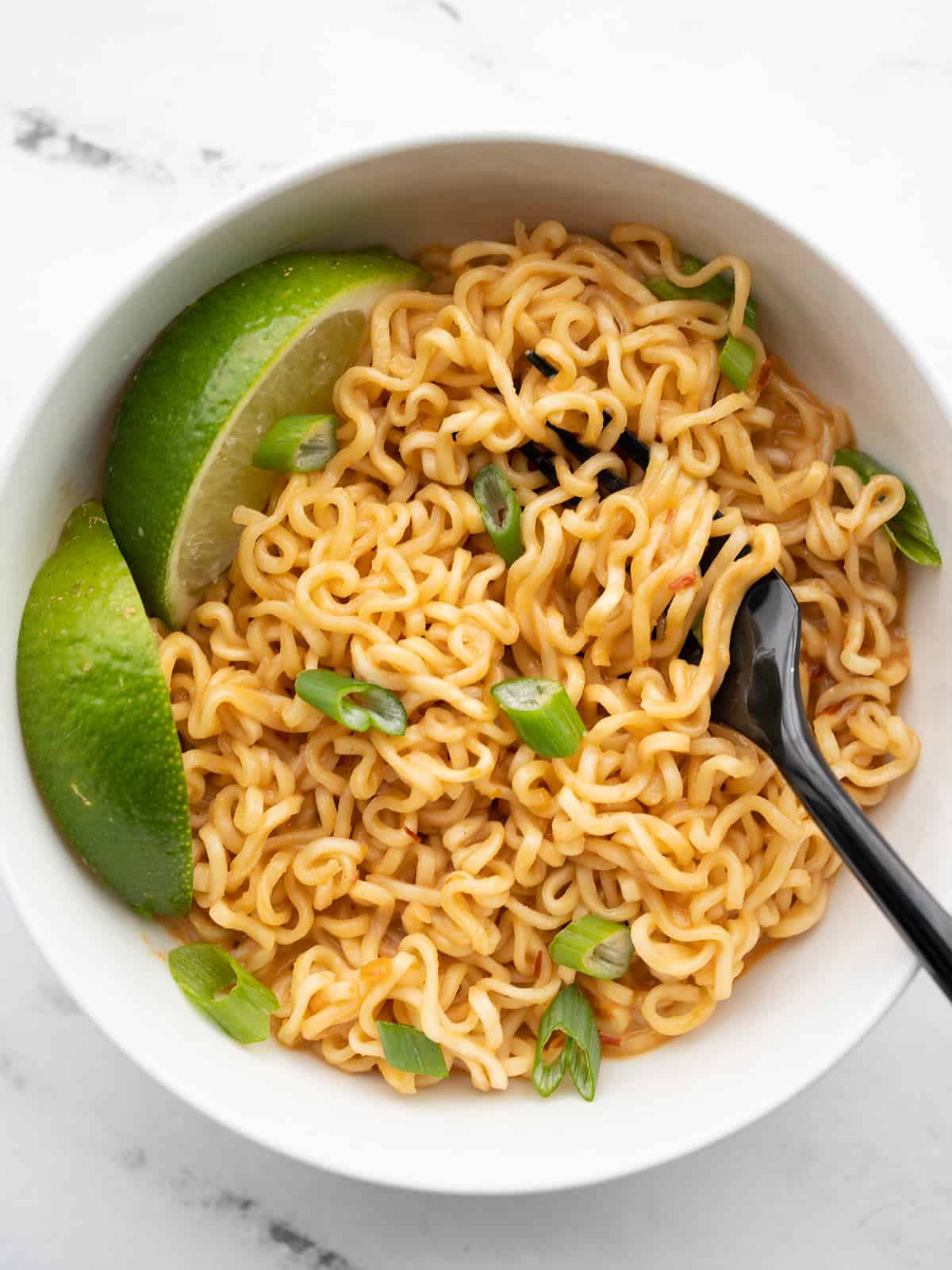 Overhead view of a bowl of spicy peanut ramen in a bowl with lime wedges