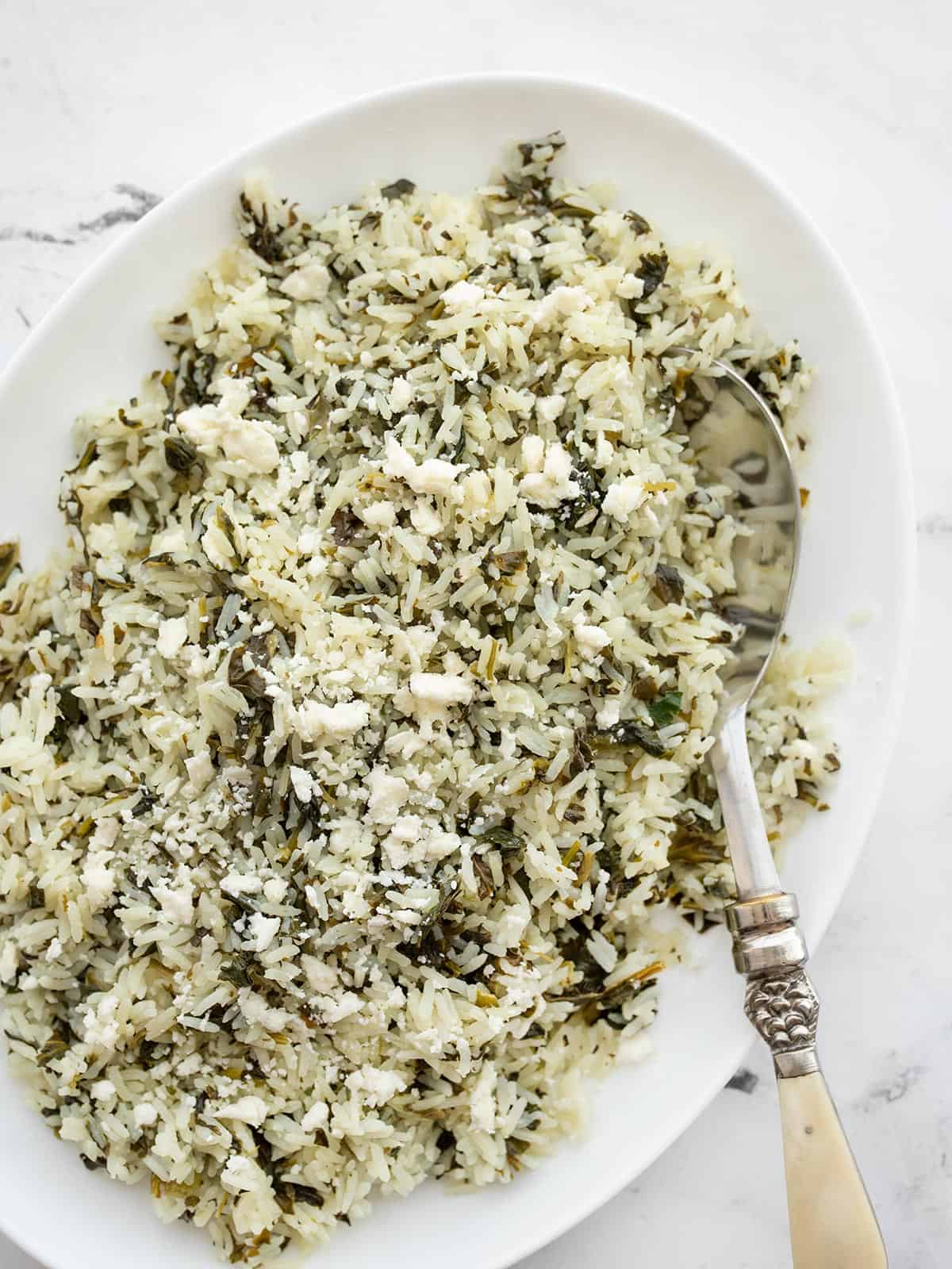 Overhead view of Spinach Rice with Feta in an oval serving dish with a serving spoon