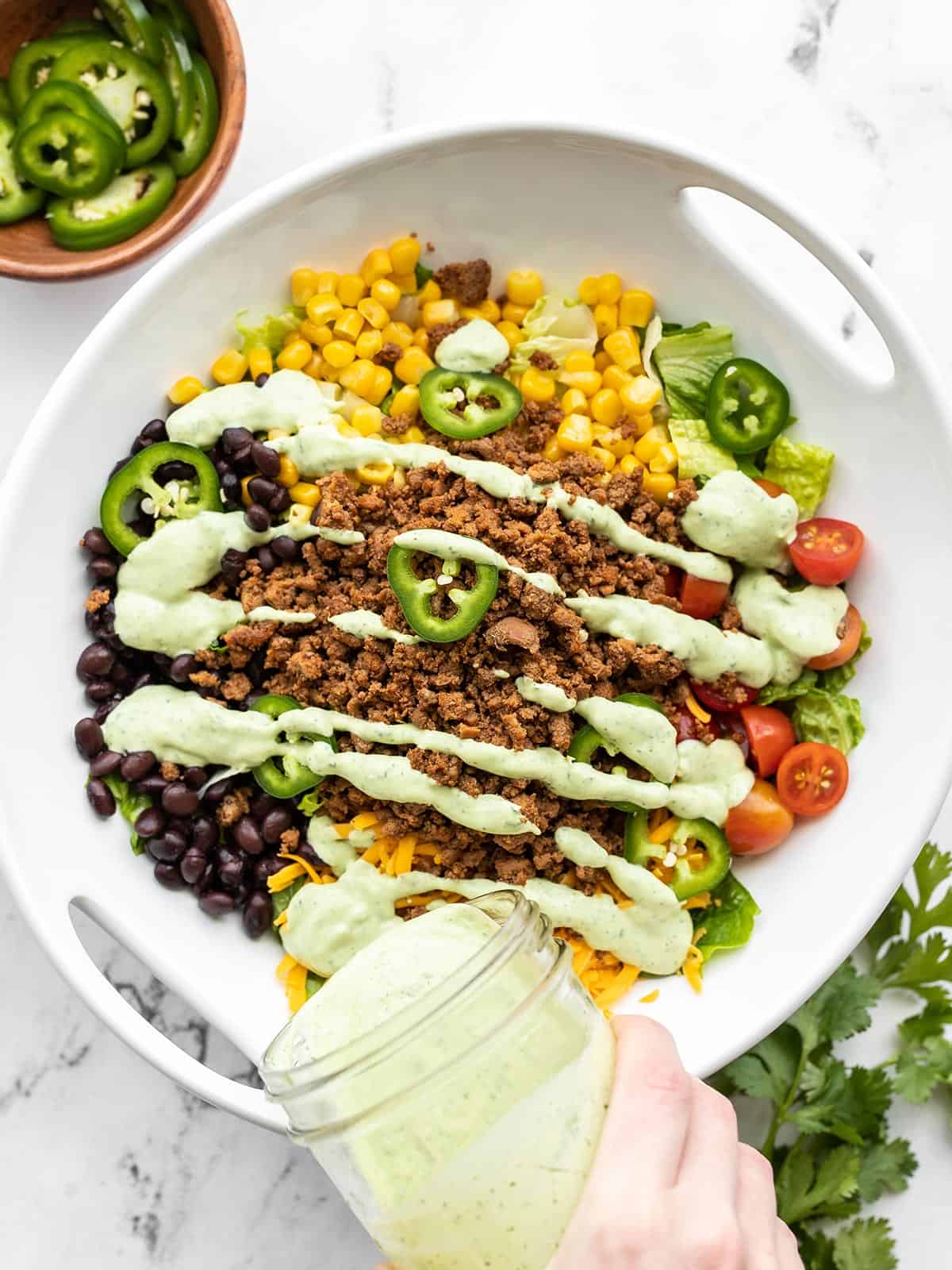 Creamy avocado dressing being poured over a turkey taco salad from a mason jar