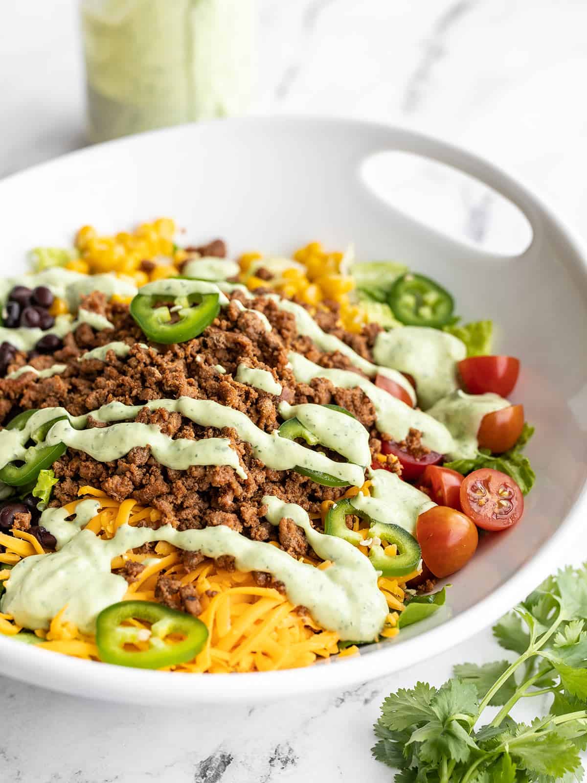 Side view of turkey taco salad in a serving bowl with the jar of dressing in the back