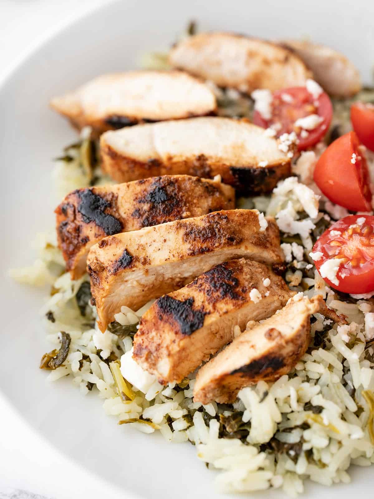 Sliced yogurt marinated chicken on a bed of spinach rice with tomatoes