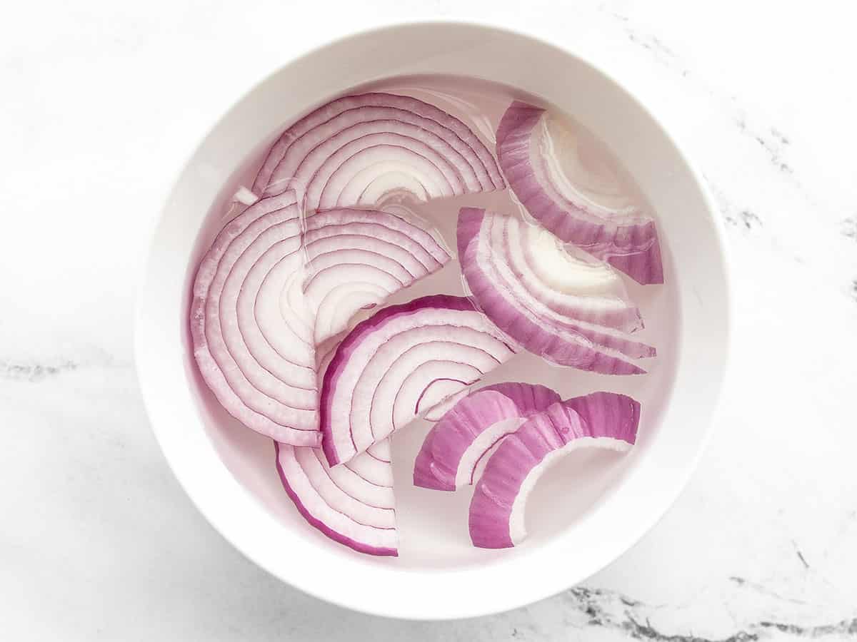 red onion slices soaking in a bowl of water