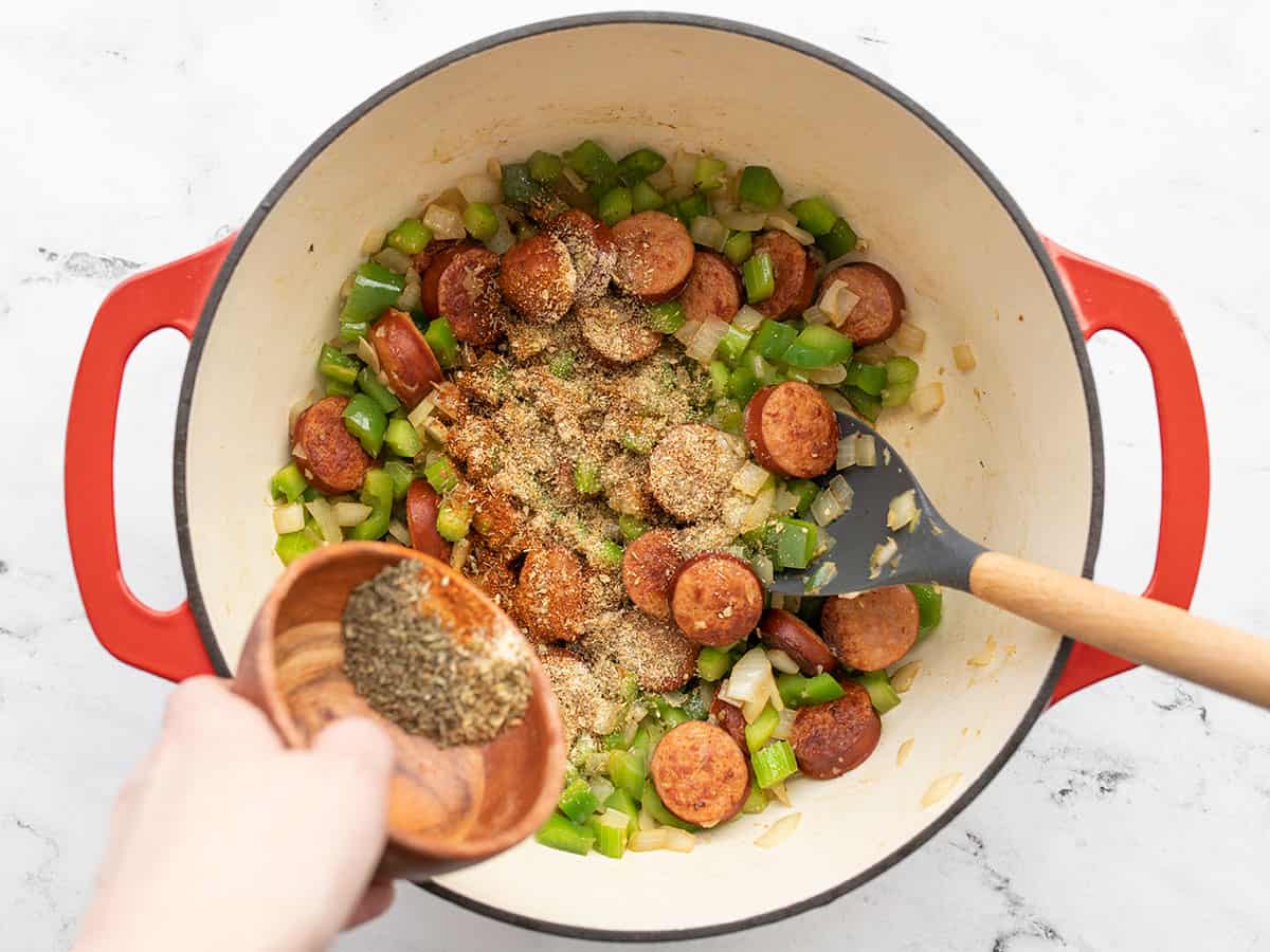 Spices being poured into the pot with sausage and vegetables