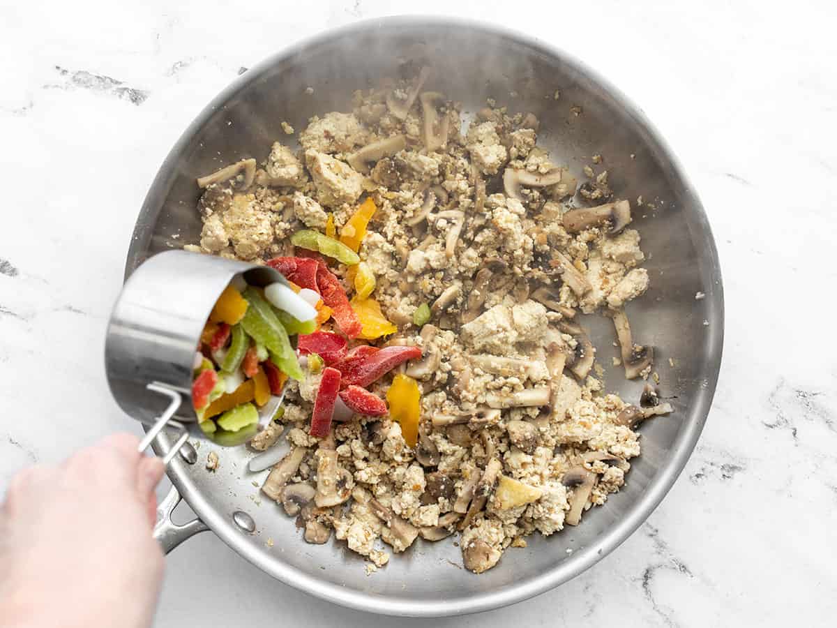 Frozen peppers and onions being added to the skillet