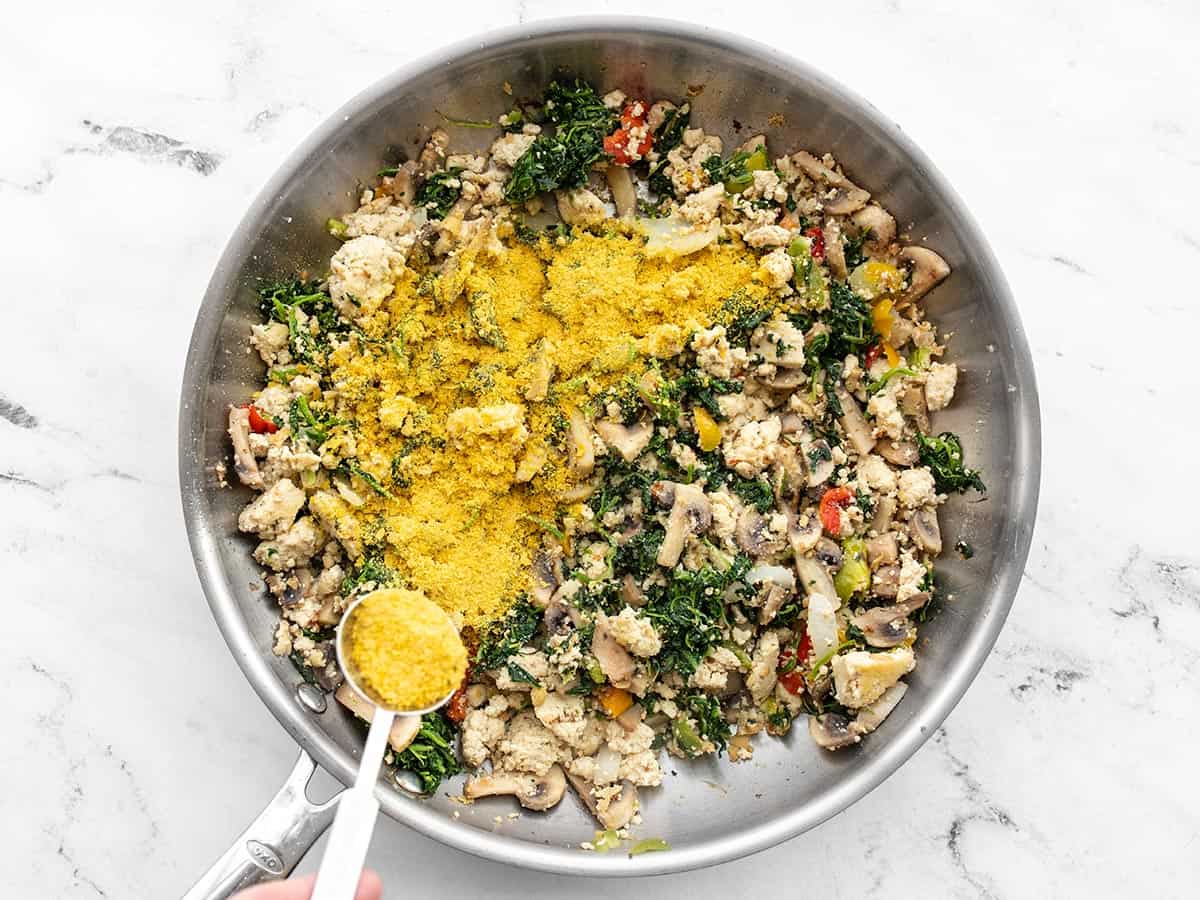 Nutritional Yeast being sprinkled over the tofu scramble in the skillet