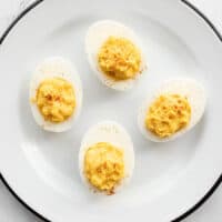 Four deviled eggs on a white plate garnished with paprika