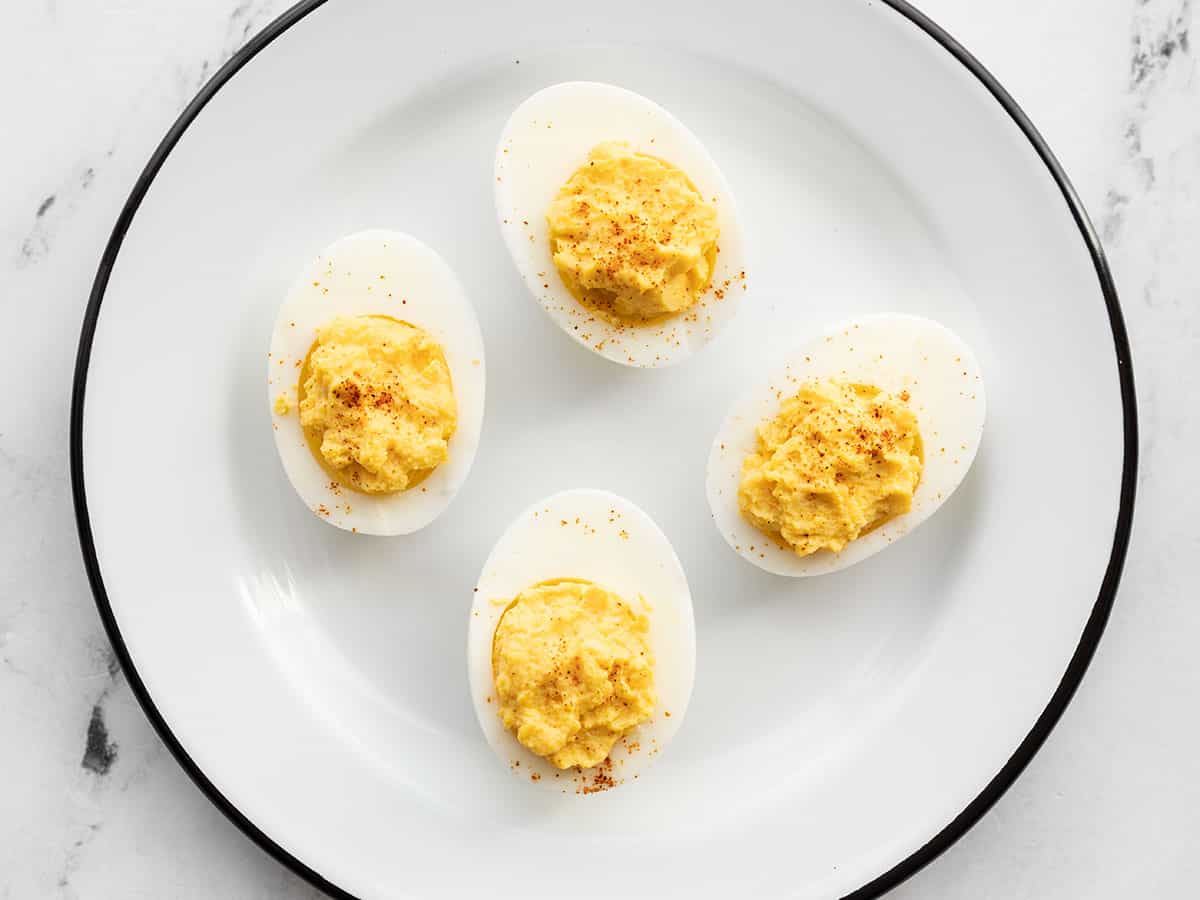 Four deviled eggs on a white plate garnished with paprika