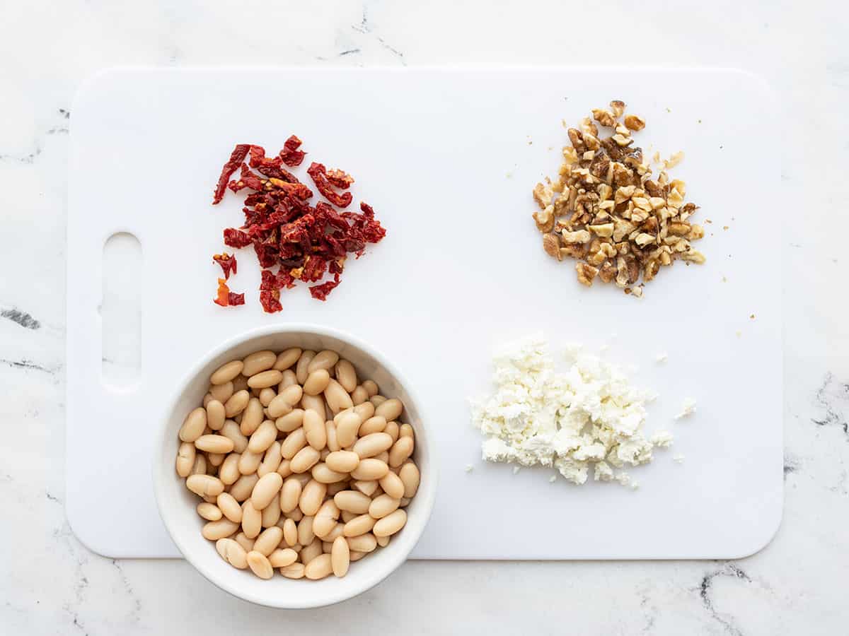 Sun dried tomatoes, walnuts, beans, and feta on a cutting board