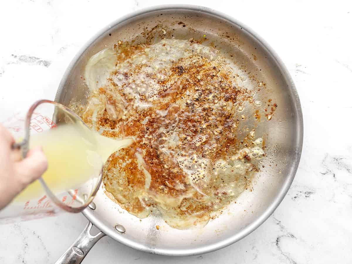 Chicken broth being poured into the skillet