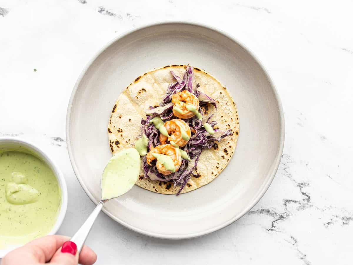 Avocado dressing being drizzled over a shrimp taco on a plate