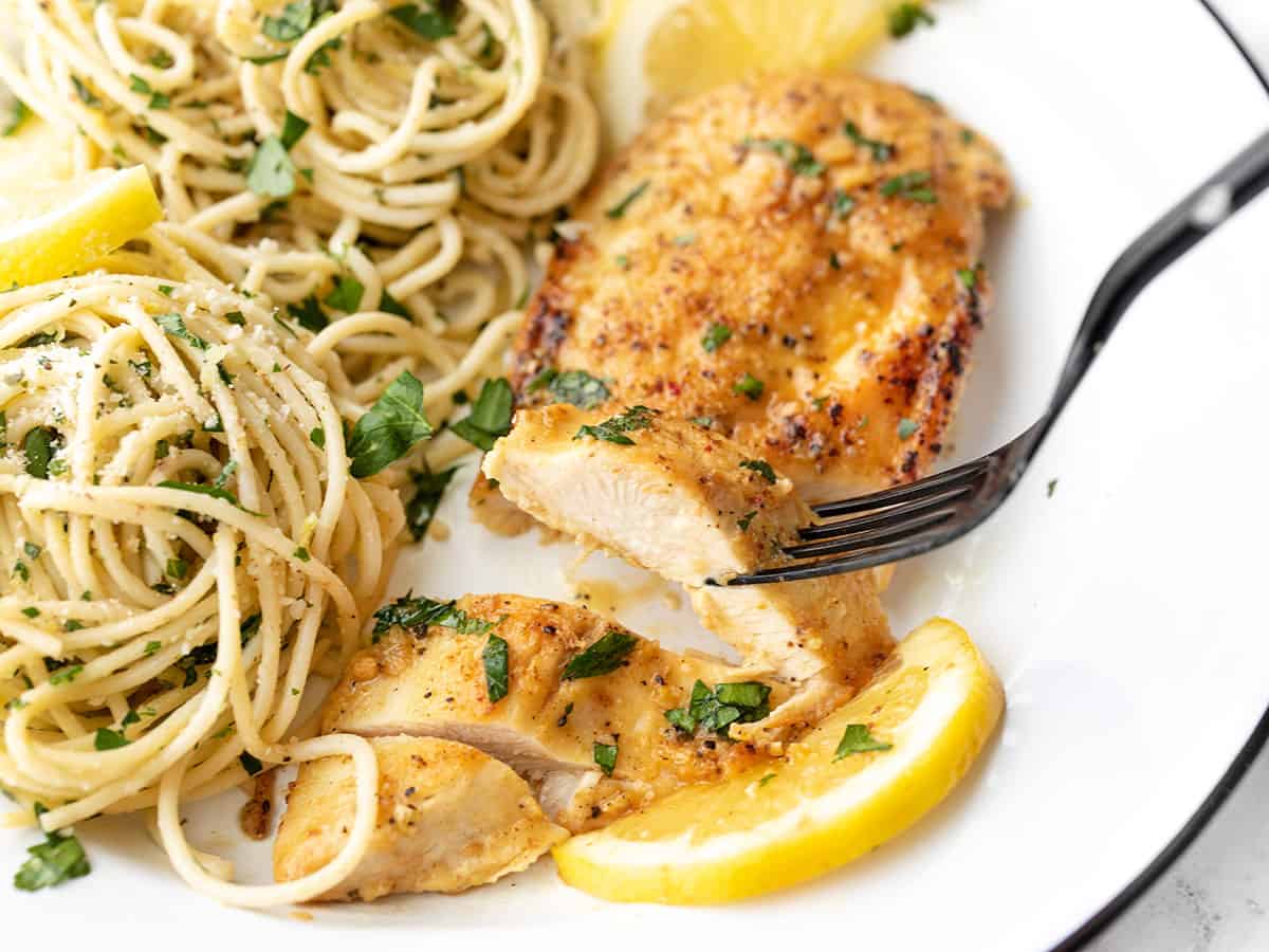 A fork lifting a slice of lemon pepper chicken from the plate