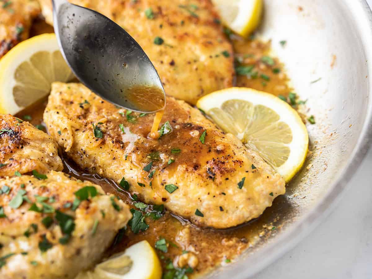 Pan sauce being spooned over a piece of lemon pepper chicken in the skillet