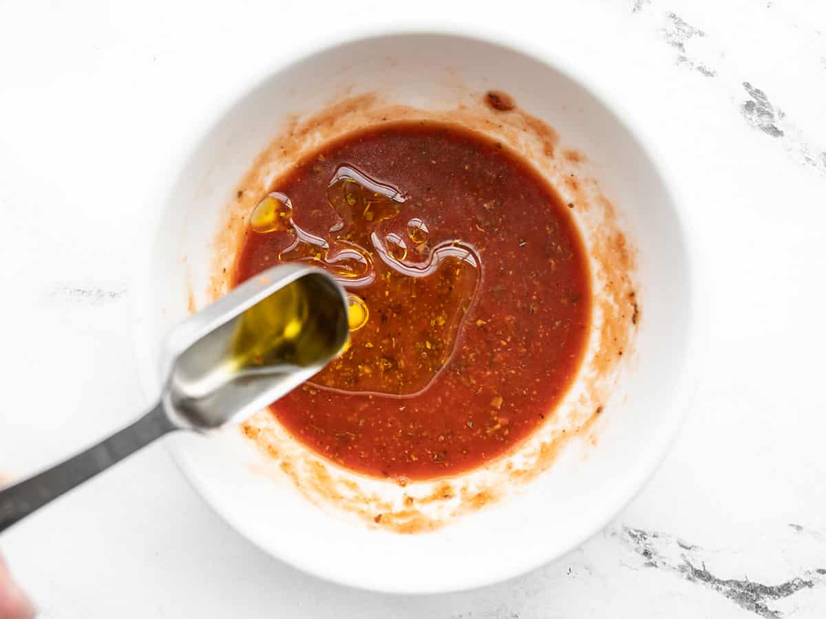 One tablespoon oil being added to tomato paste mixture in the bowl