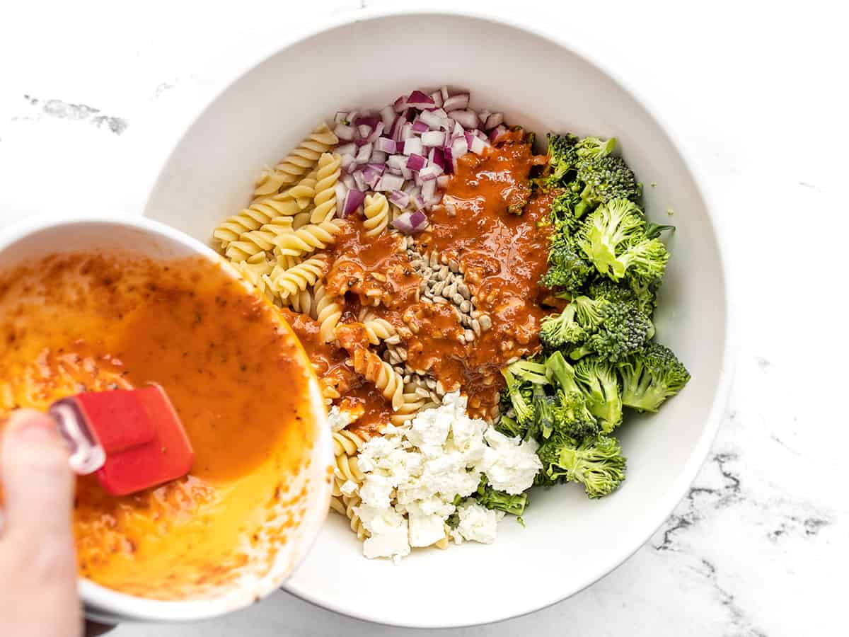 Tomato vinaigrette being poured over the pasta salad ingredients