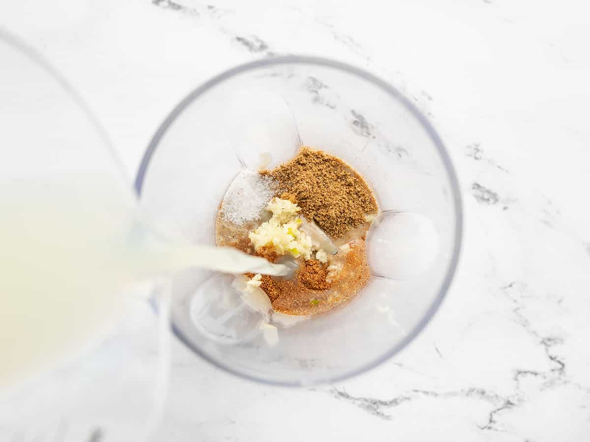 lemon juice being poured into a blender containing the rest of the dressing ingredients