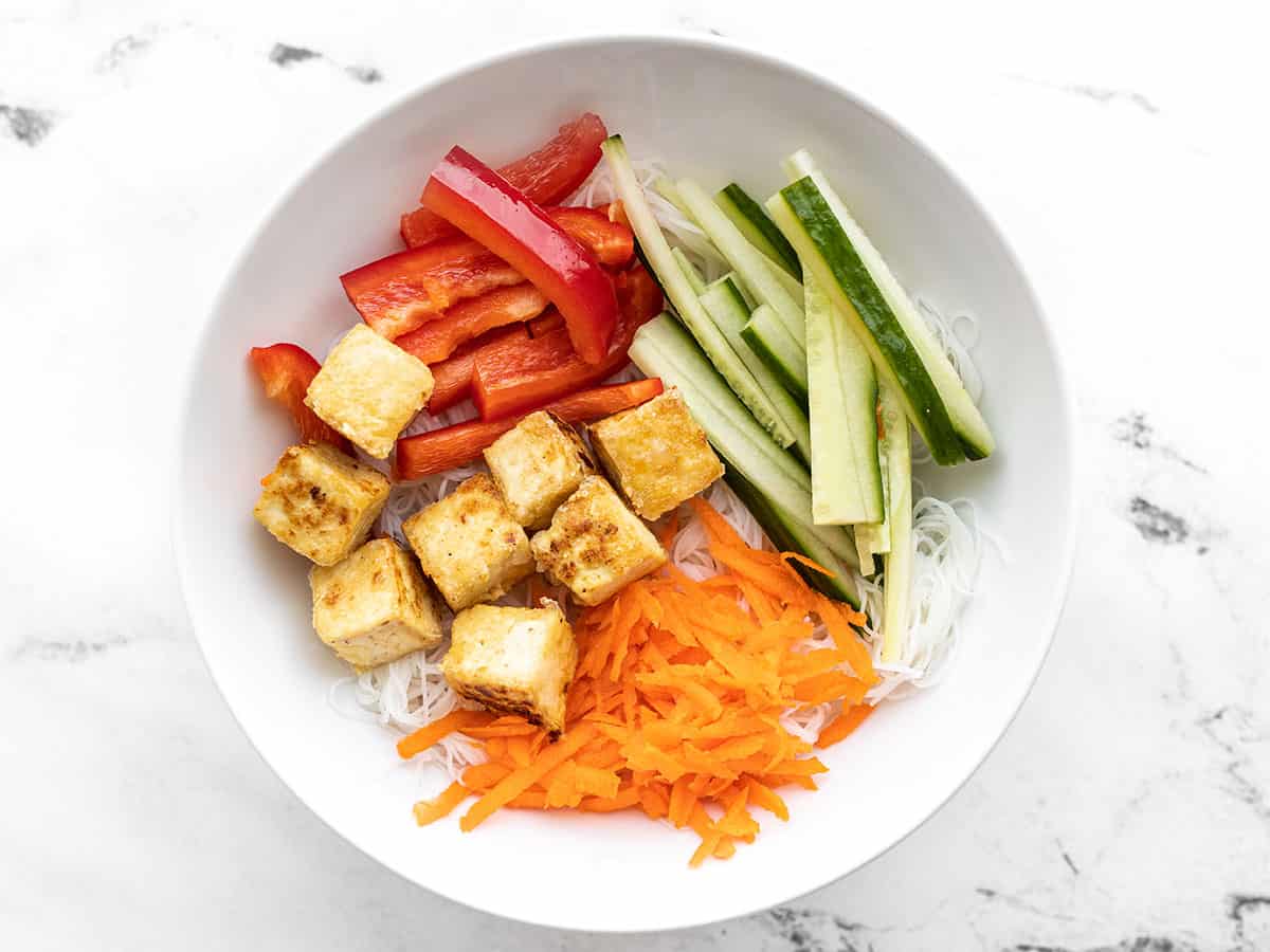 rice noodles in a bowl topped with tofu, bell pepper, cucumber, and carrots