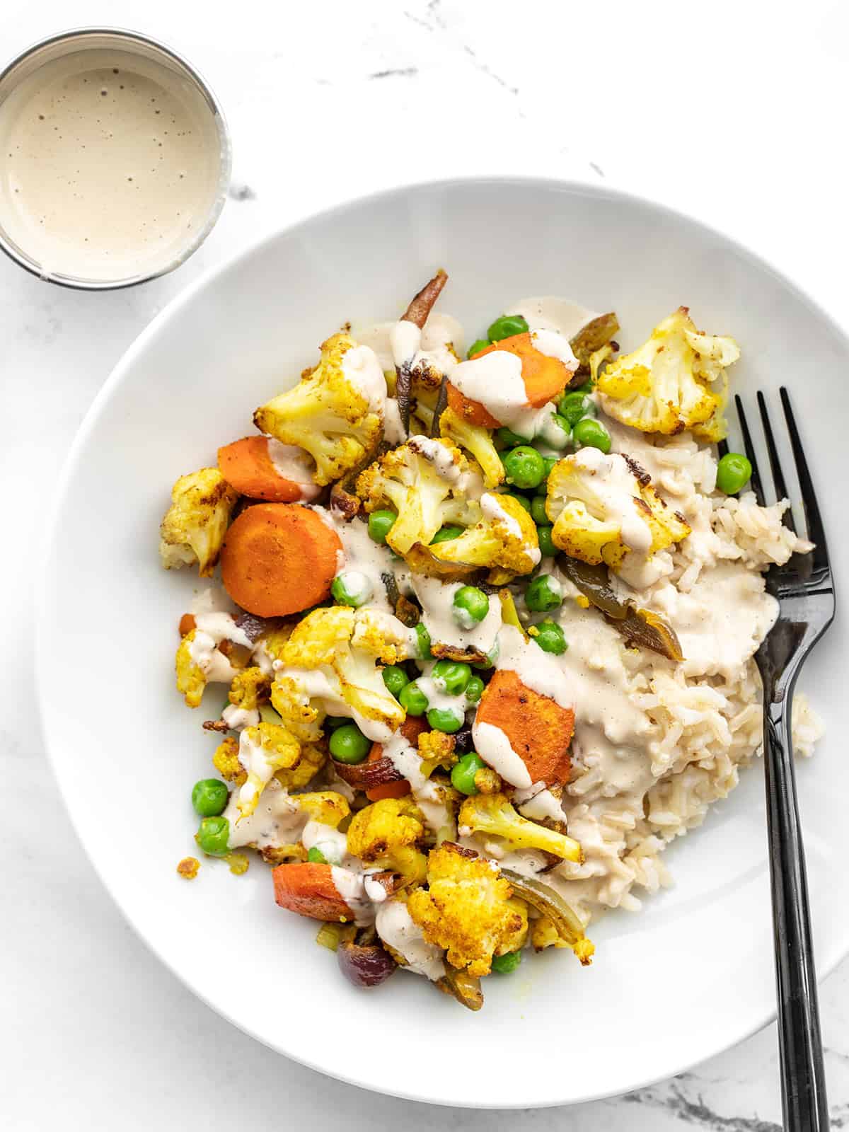 Overhead view of curry roasted vegetable bowls with a dish of dressing on the side