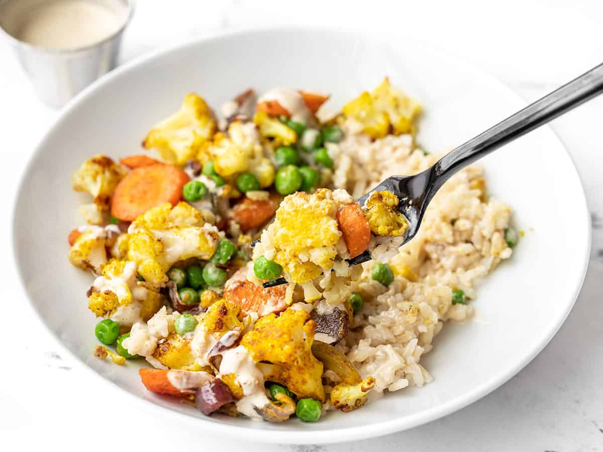 Side view of a fork lifting a bite out of the curry roasted vegetable bowls