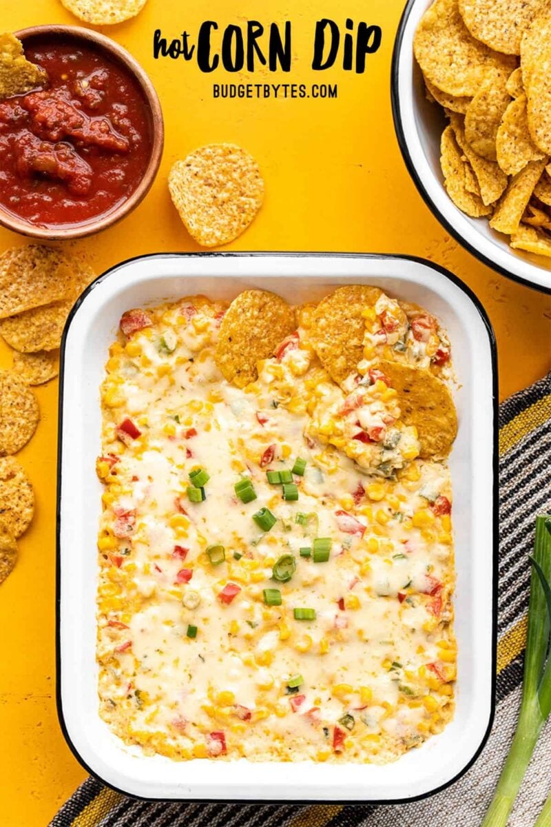 Hot corn dip in a rectangular baking dish, chips and salsa on the sides