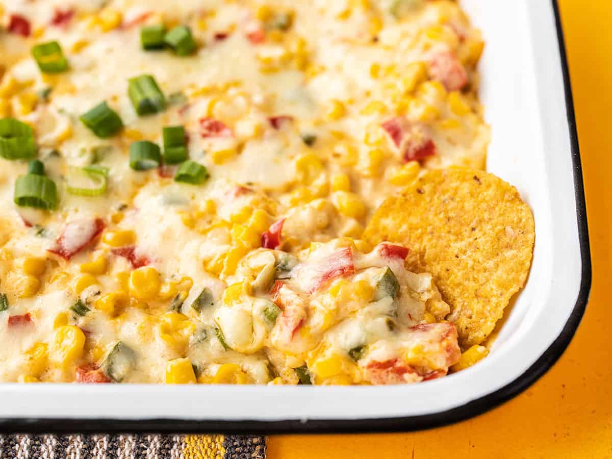 Close up of a chip dipped into the corner of the hot corn dip casserole dish