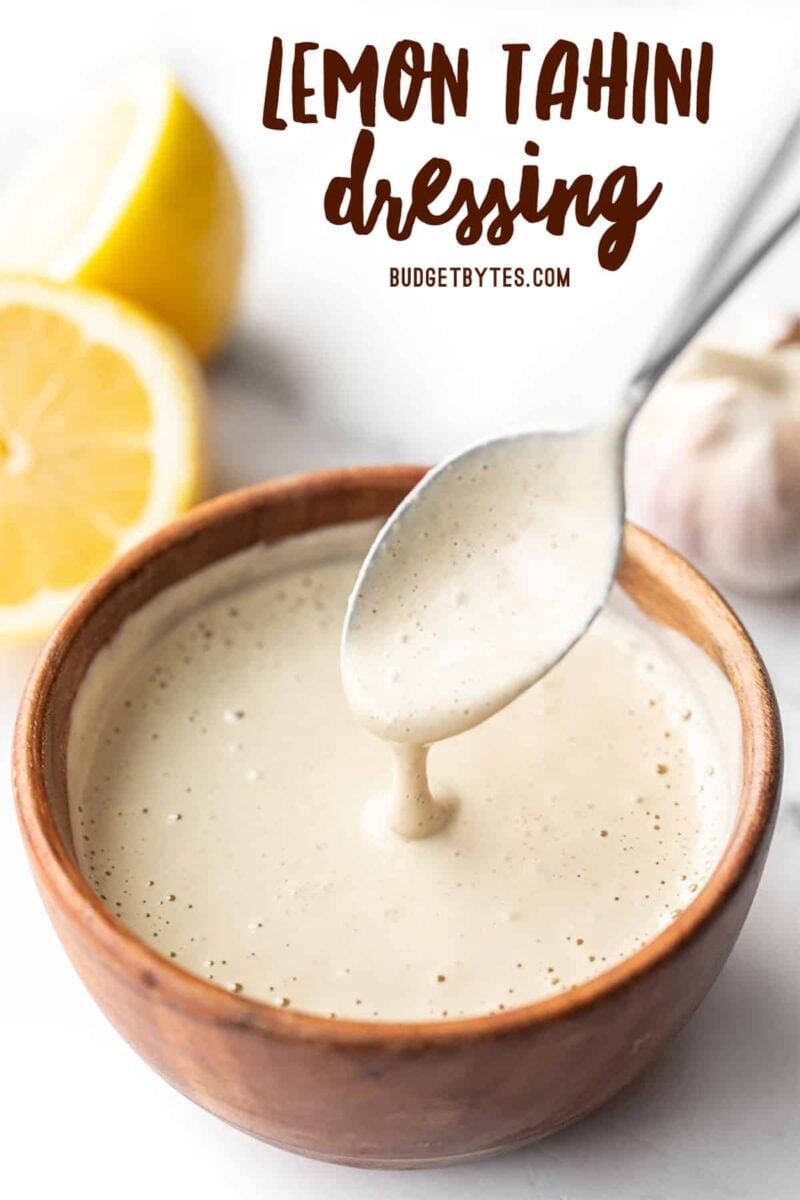 Lemon tahini dressing dripping off a spoon into a wooden bowl