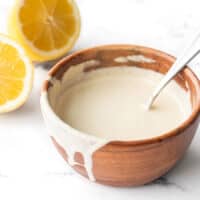 Side view of a wooden bowl with lemon tahini dressing, some dripping down the side