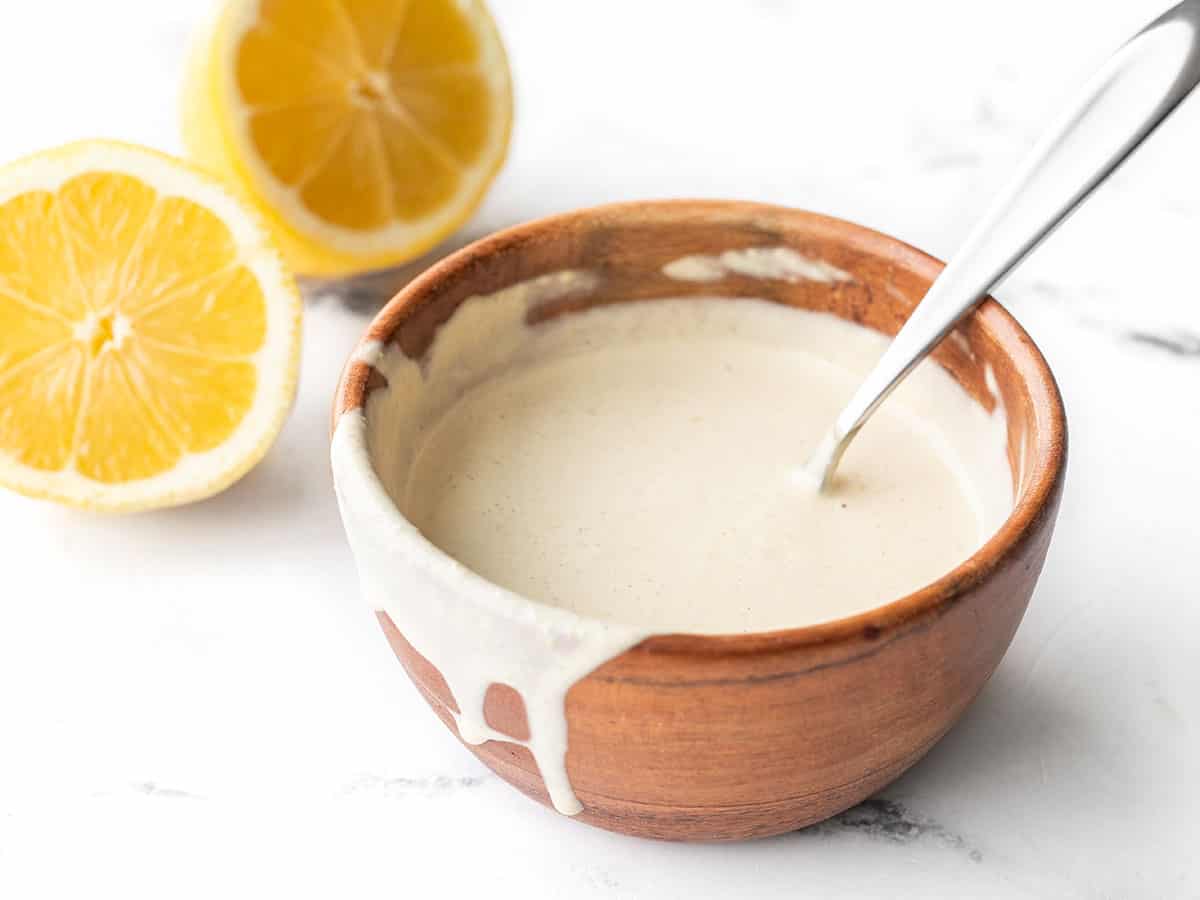 Side view of a wooden bowl with lemon tahini dressing, some dripping down the side