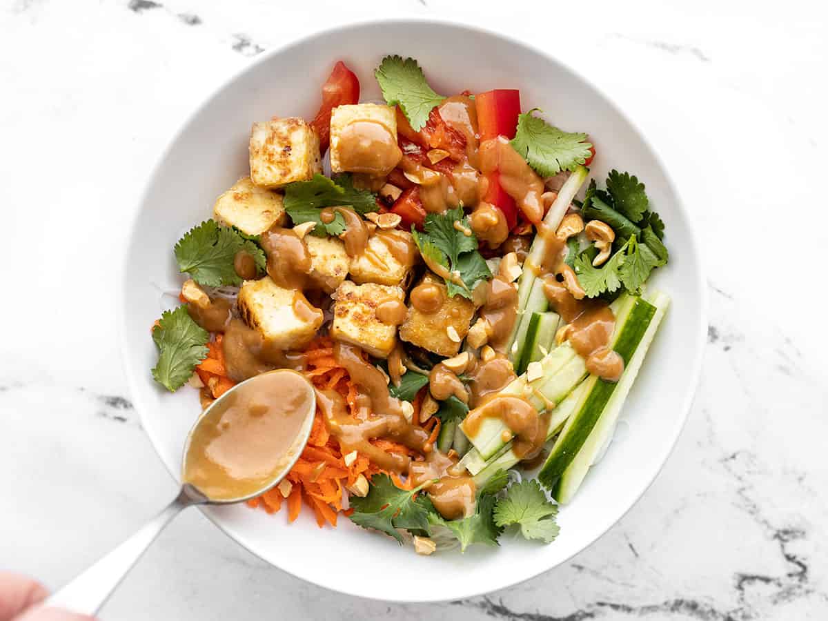 Peanut lime dressing being drizzled over a peanut tofu noodle bowl