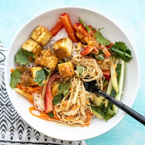 Half-stirred peanut tofu noodle bowl with a fork in the center