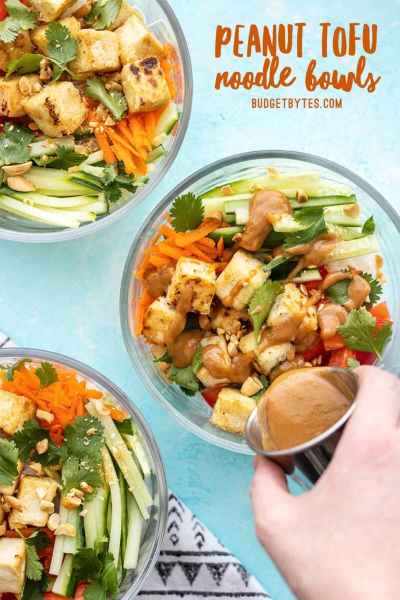 Three peanut tofu noodle bowls with peanut lime dressing being poured over one