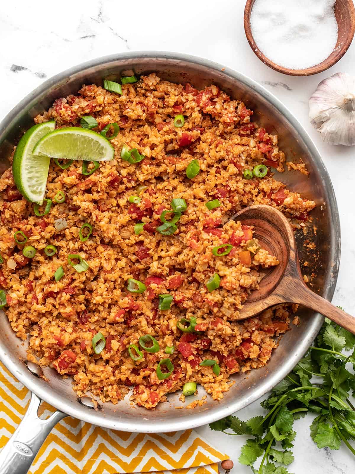 Overhead view of a skillet full of Southwest Cauliflower Rice garnished with lime and a bowl of salt on the side