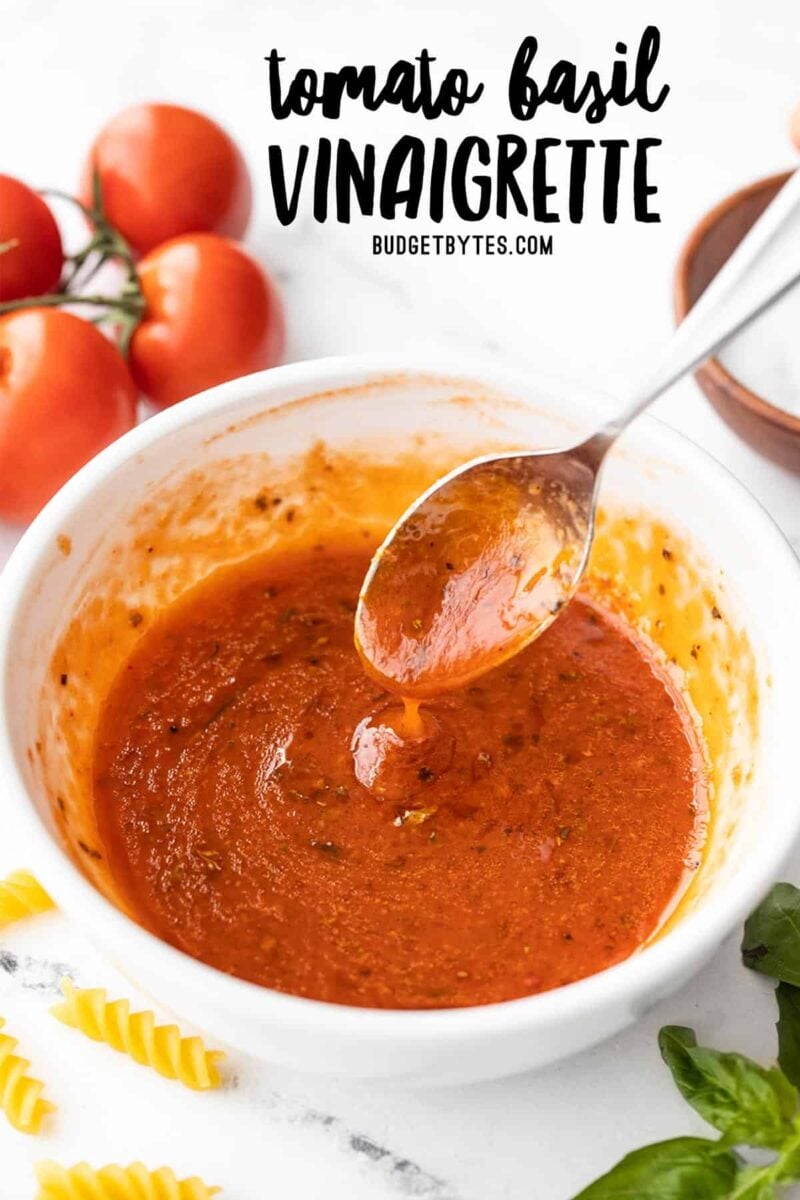 side view of a spoon drizzling tomato basil vinaigrette into a bowl, title text at the top