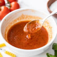 Side view of a bowl of tomato basil vinaigrette with a spoon dripping the dressing into a bowl